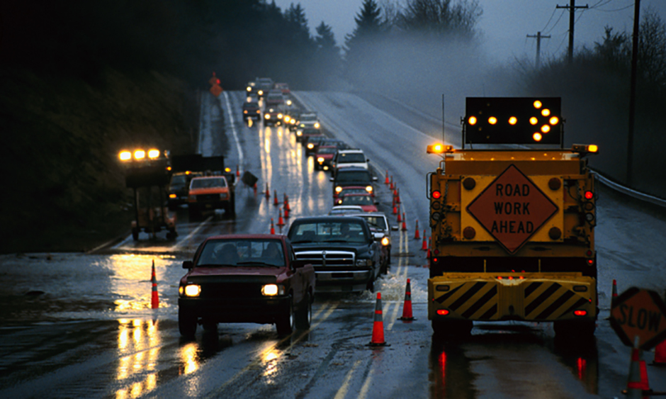 Cars pass through a construction zone on a rainy night