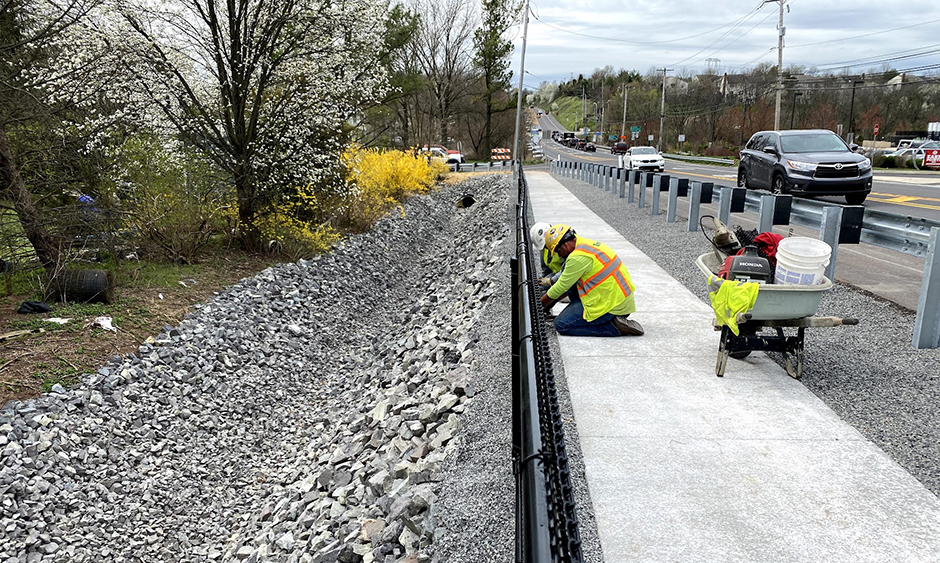 Workers installing a new sidewalk and fencing alongside a road