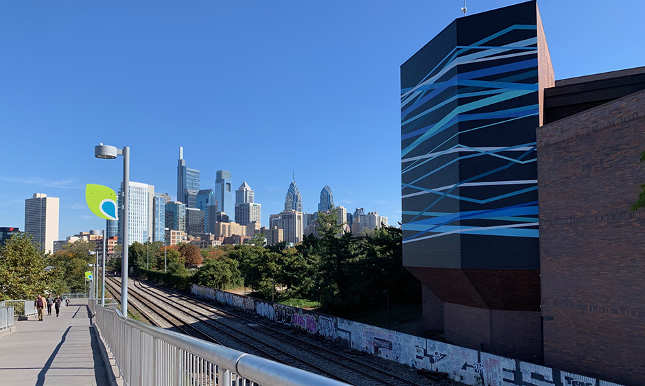A photo of the Schuylkill River Trail with railroad tracks to the right and the Philadelphia skyline in the distance