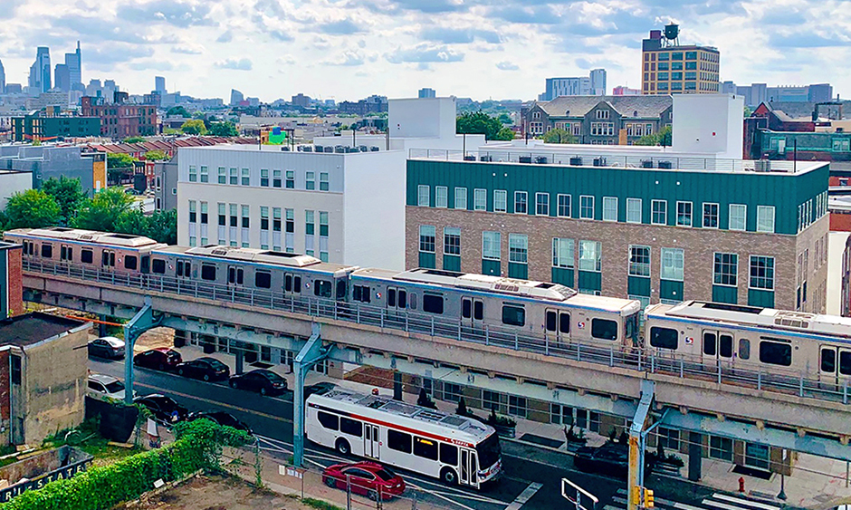 The Market-Frankford subway on elevated tracks over a street that has a SEPTA bus on it. The Philadelphia Center City skyline is in the distance