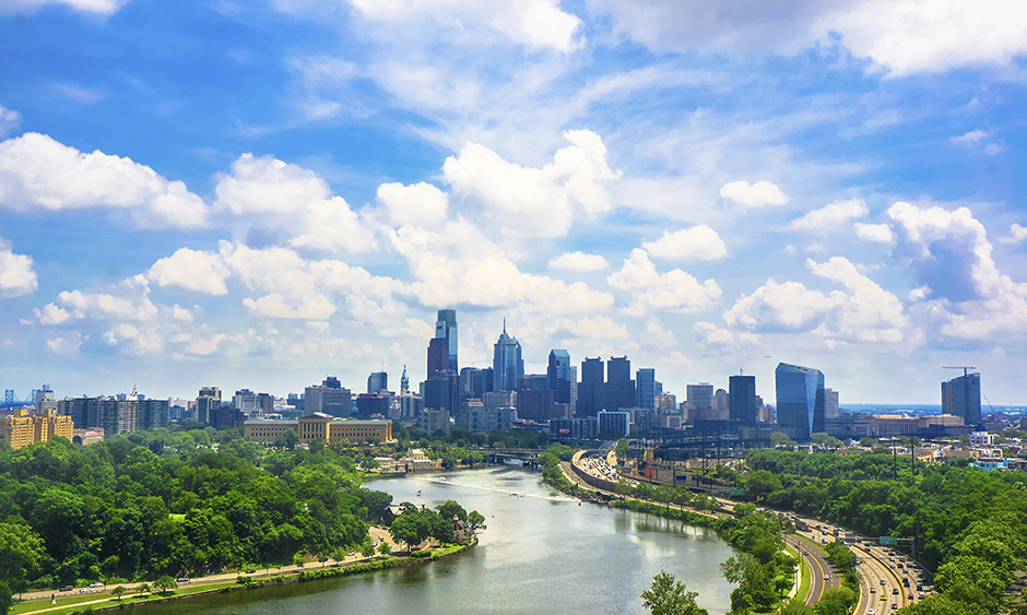 The Schuylkill River with the Philadelphia skyline in the distance. The blue sky is full of fluffy white clouds