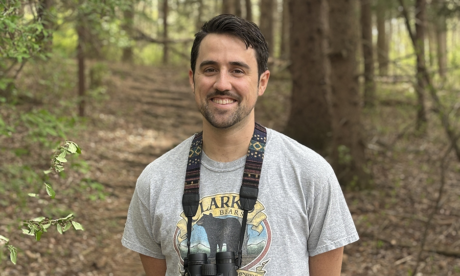 DVRPC staff member Chris Mulroy poses for a photo in the woods with binoculars around his neck