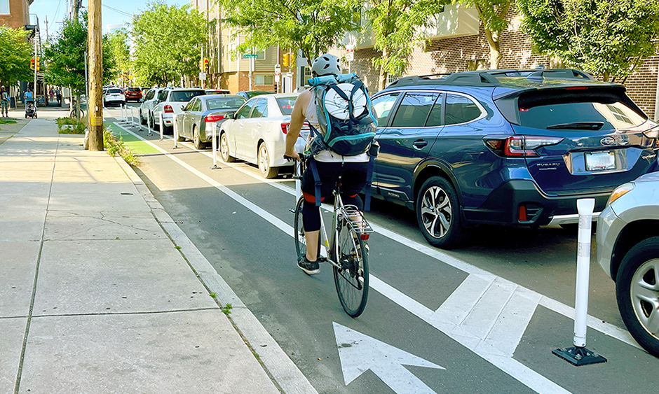 A photo of a person riding a bicycle in a parking separated bike lane