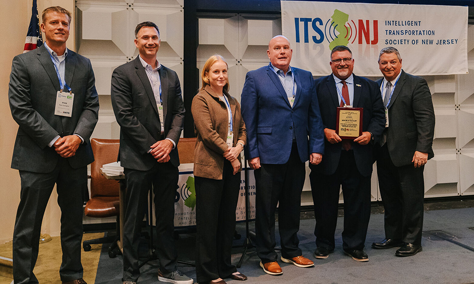 Six people stand together for a photo. One person holds an award plaque.