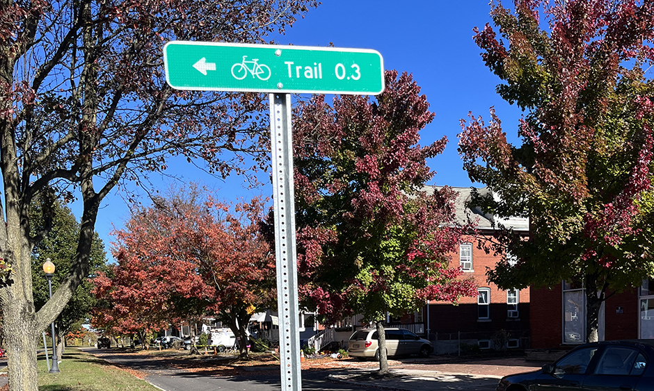 A street sign in a residential area that indicates a bike trail is 0.3 miles away